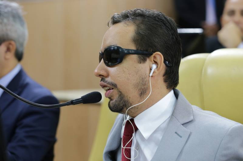 Vereador Lucas Aribé sentado falando ao microfone