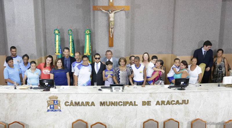 Vereador Lucas Aribé em pé rodeado dos componentes da mesa diretiva, vereadores presentes à Sessão Especial e pessoas com autismo