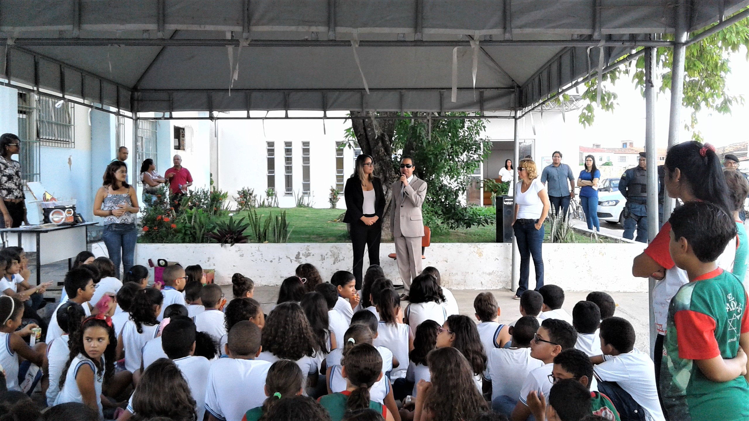 Vereador Lucas Aribé em pé ao lado da vereadora Kitty Lima falando para crianças que estão sentadas no chão