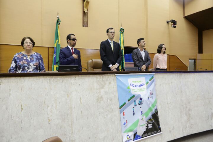 Os membros da mesa estão de pé atentos a execução do Hino Nacional - Foto 1