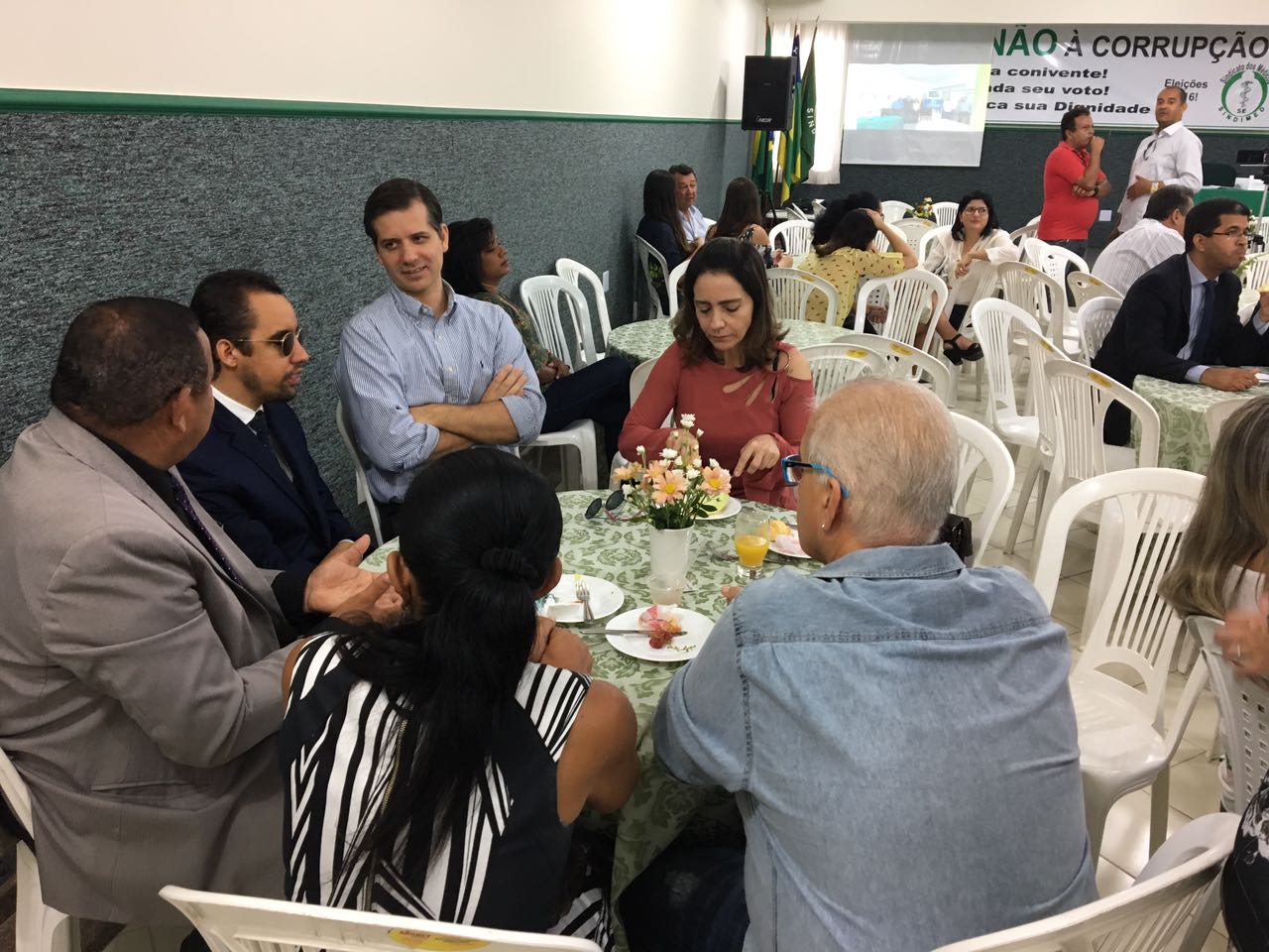 #PraCegoVer: Vereadores estão sentados à mesa dentro do auditório enquanto aguardavam o evento começar