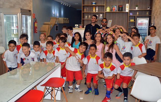 #PraCegoVer: O vereador Lucas Aribé está posando para a foto juntamente com o proprietário do Il Sordo, Breno Oliveira, e cerca de 30 crianças fazendo o sinal da gelateria