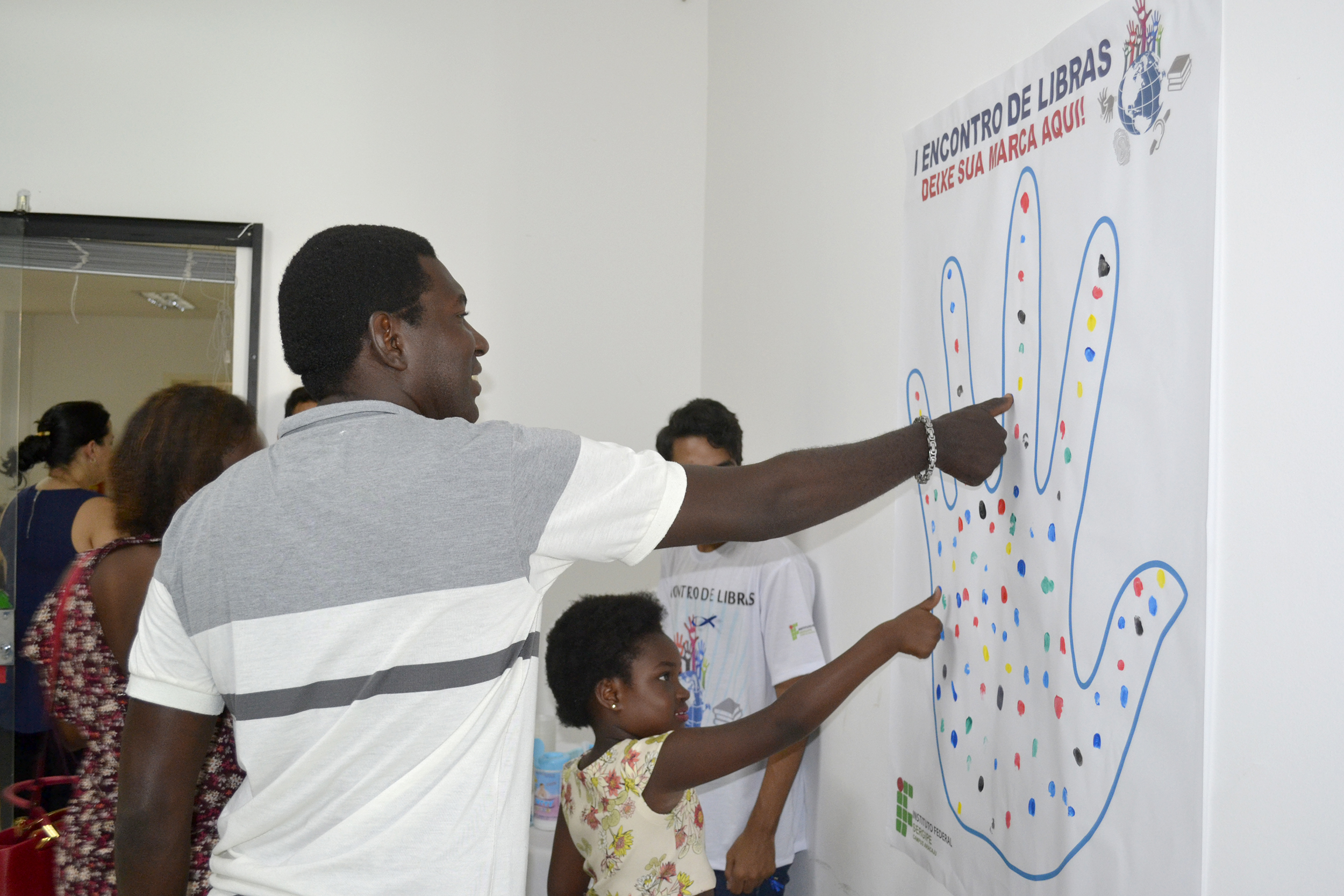 #PraCegoVer - Pai e filha deixam suas digitais em painel interativo do IFS