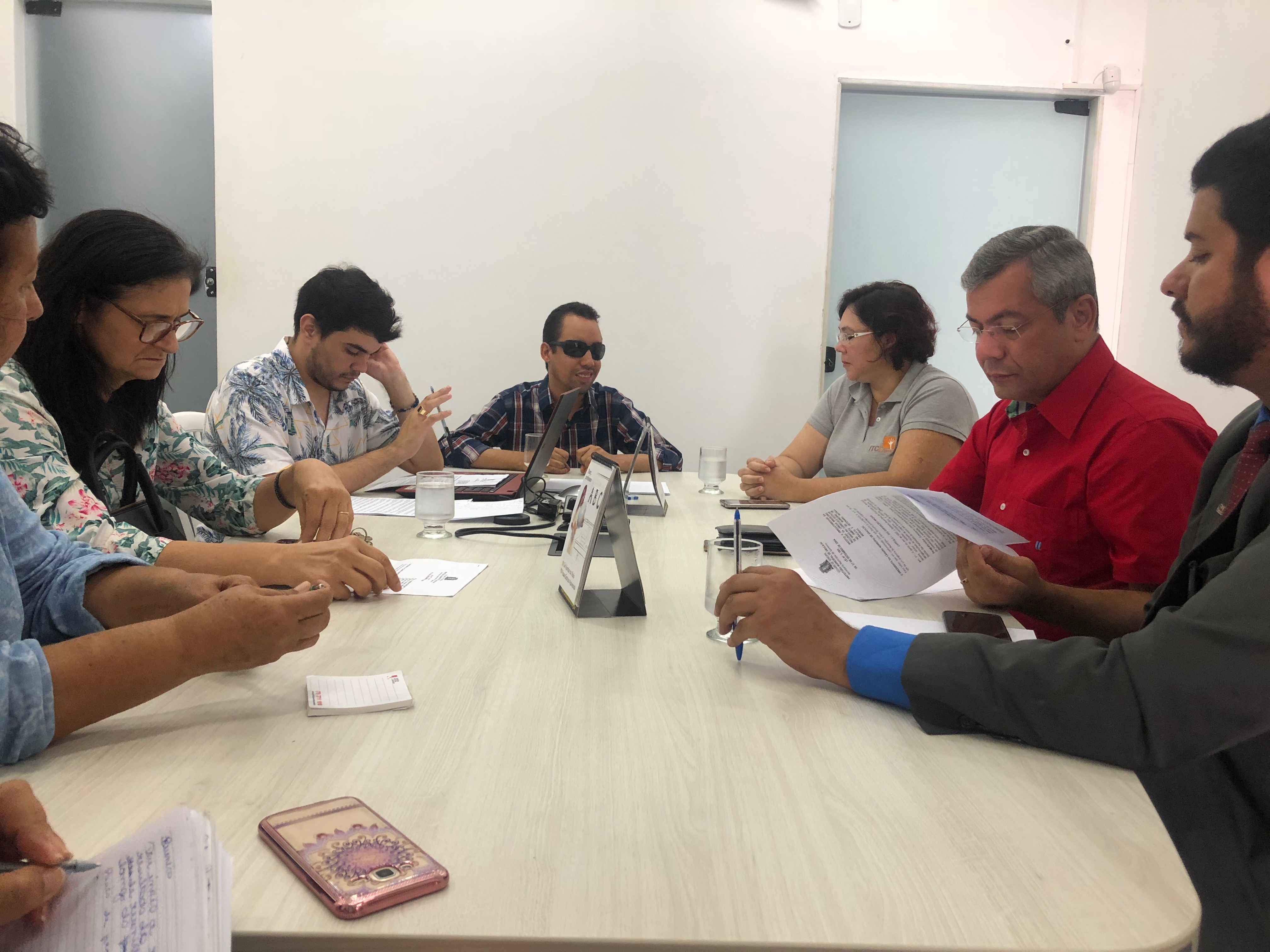 #PraCegoVer: A foto mostra oito pessoas reunidas ao redor de uma mesa dialogando