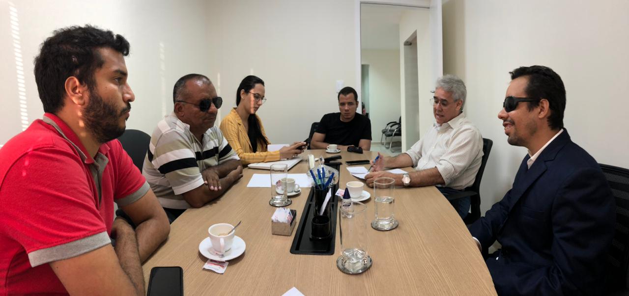 #PraCegoVer: O vereador Lucas Aribé está reunido com mais quatro pessoas, sendo uma mulher e todos estão sentados ao redor de uma mesa