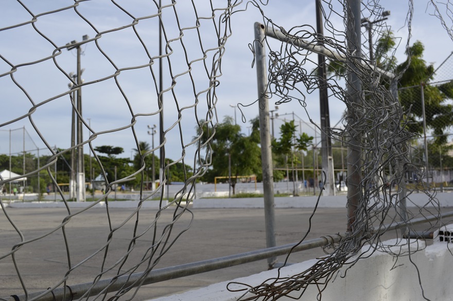 #PraTodoMundoVer Alambrado da quadra quebrado com praça ao fundo desfocada