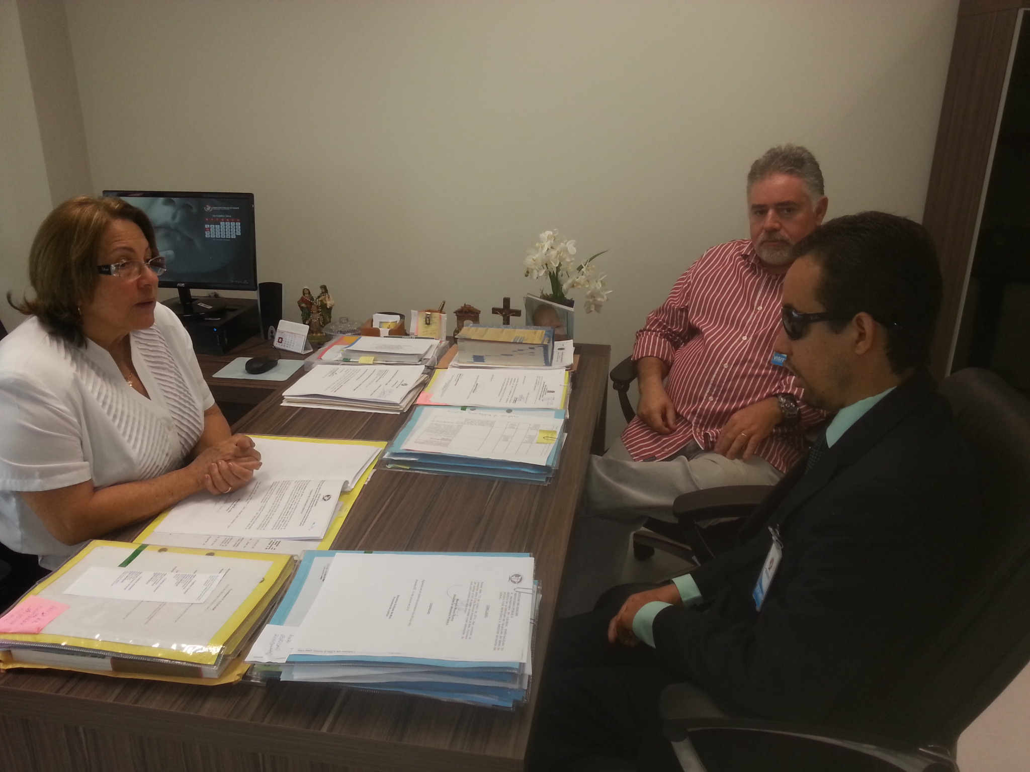 Na imagem, a promotora Berenice Melo, Augusto Carvalho e Lucas estão em frente a uma mesa